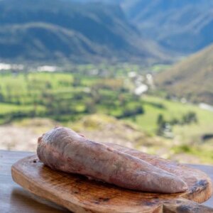 Lengua de ternera fresca entera sobre una tabla de madera rústica con el Valle de Benasque al fondo